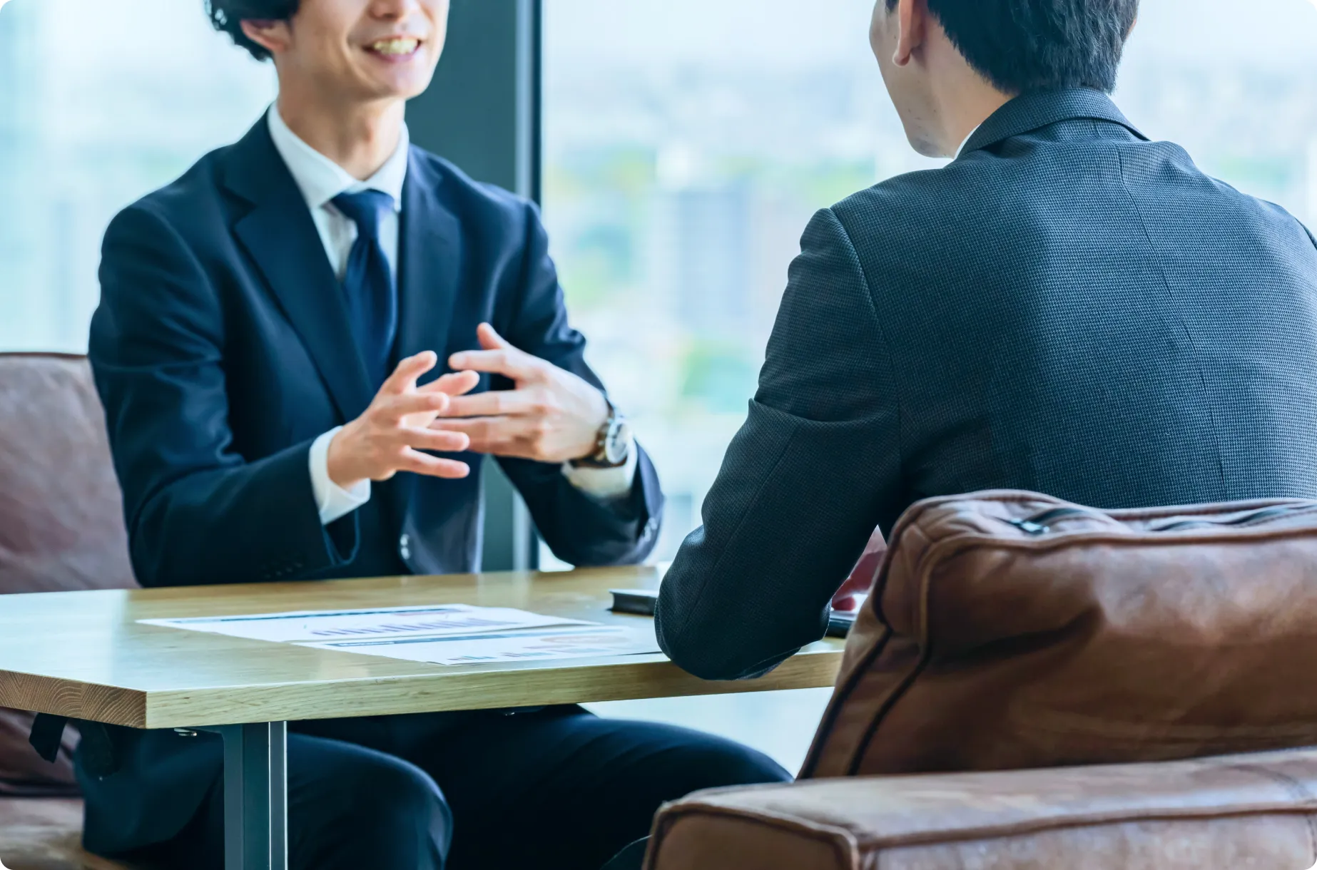 スーツを着用した男性二人が机を挟んで座り話し合っている様子