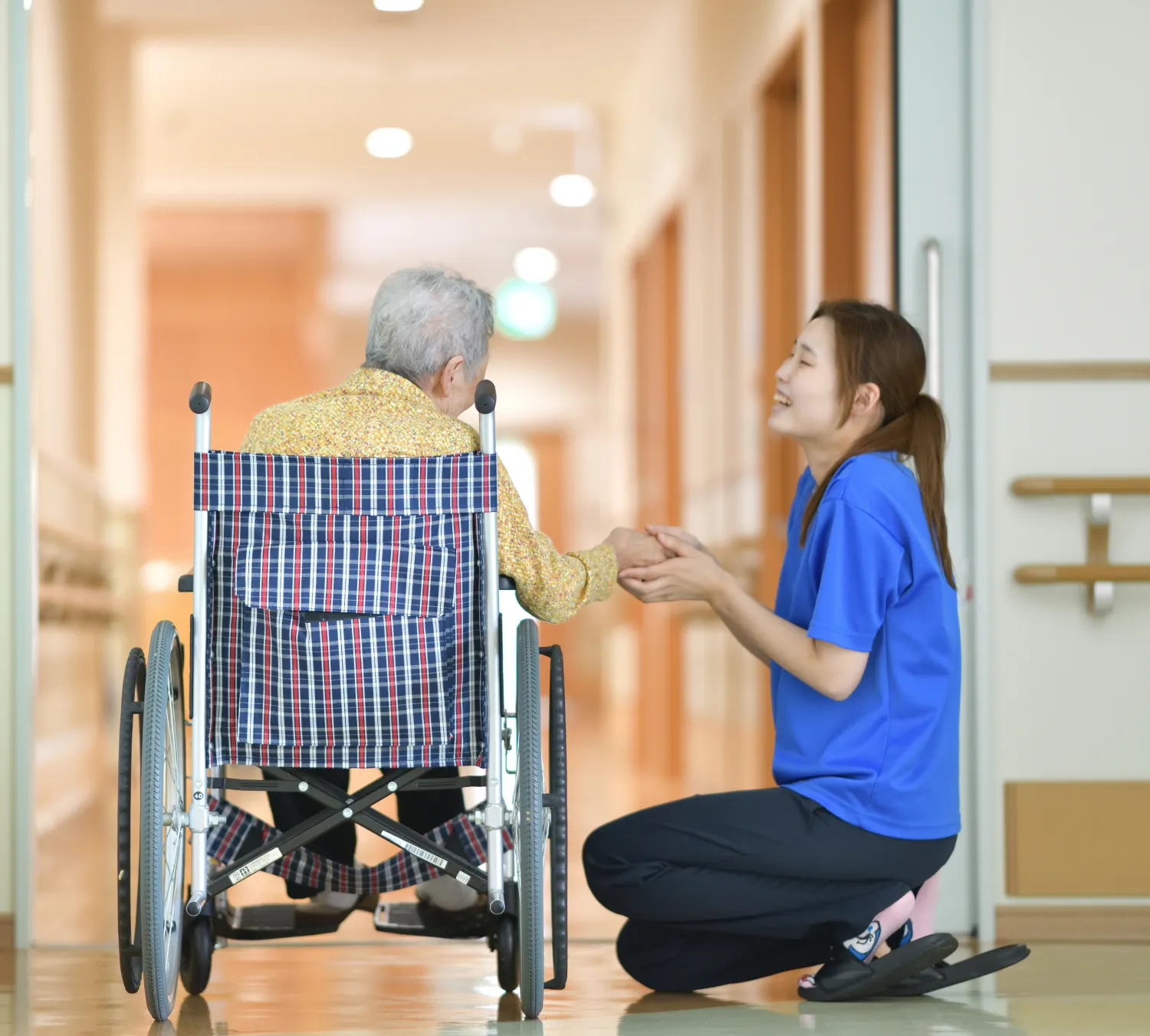 廊下で車椅子に乗った老人の手を握る介護士